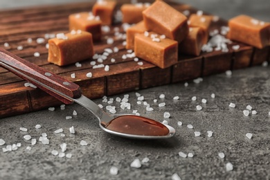 Spoon with delicious caramel sauce, salt and candies on table