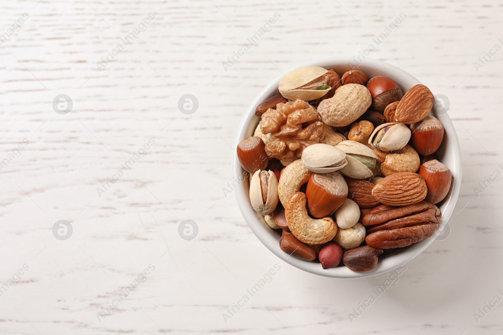 Photo of Bowl with organic mixed nuts on white wooden background, top view. Space for text