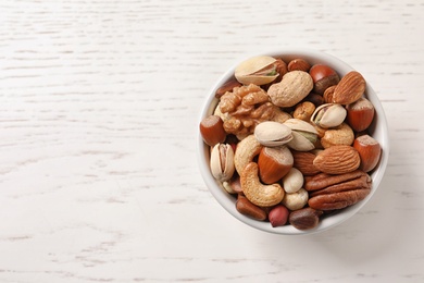 Bowl with organic mixed nuts on white wooden background, top view. Space for text