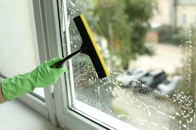 Photo of Woman cleaning glass with squeegee indoors, closeup