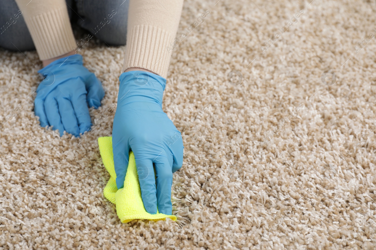 Photo of Woman in rubber gloves cleaning carpet with rag indoors, closeup. Space for text