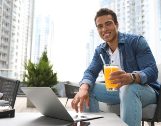 Portrait of handsome young African-American man with laptop and glass of juice in outdoor cafe