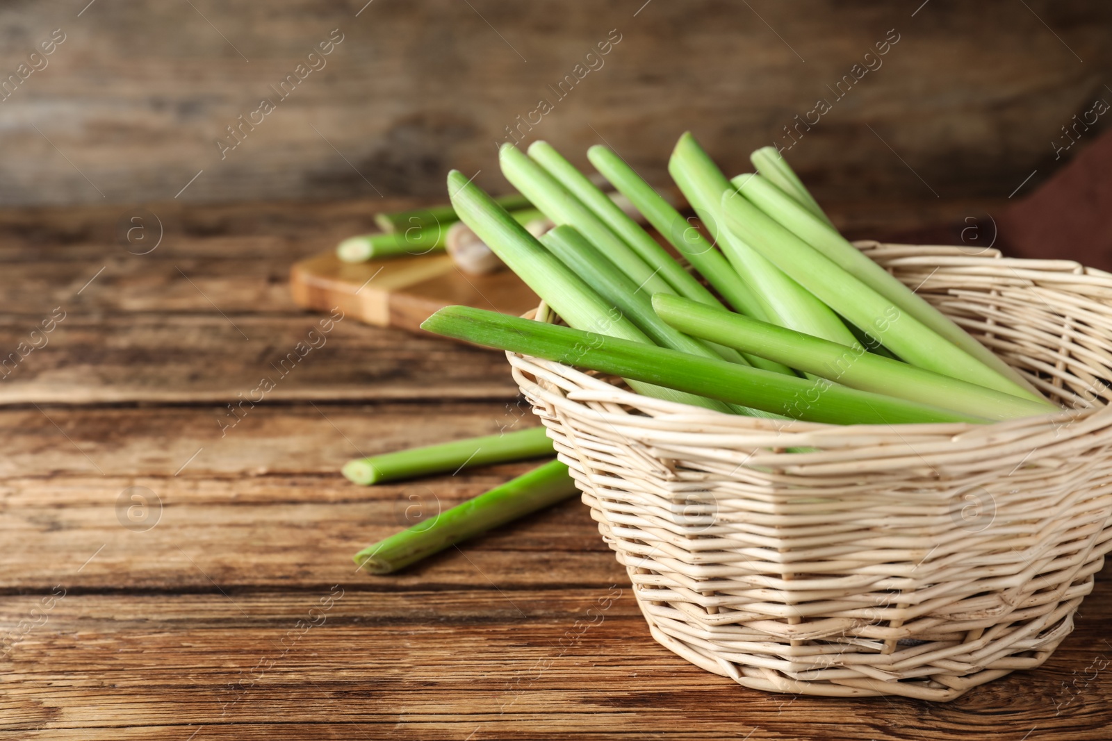 Photo of Fresh lemongrass in wicker bowl on wooden table, space for text