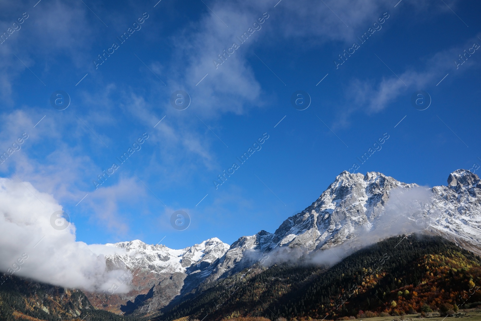 Photo of Picturesque landscape of high mountains covered with thick mist under blue sky on autumn day