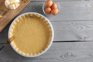 Making quiche. Baking dish with fresh dough and ingredients on grey wooden table, flat lay. Space for text