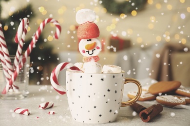 Photo of Funny marshmallow snowman in cup of hot drink on light grey table