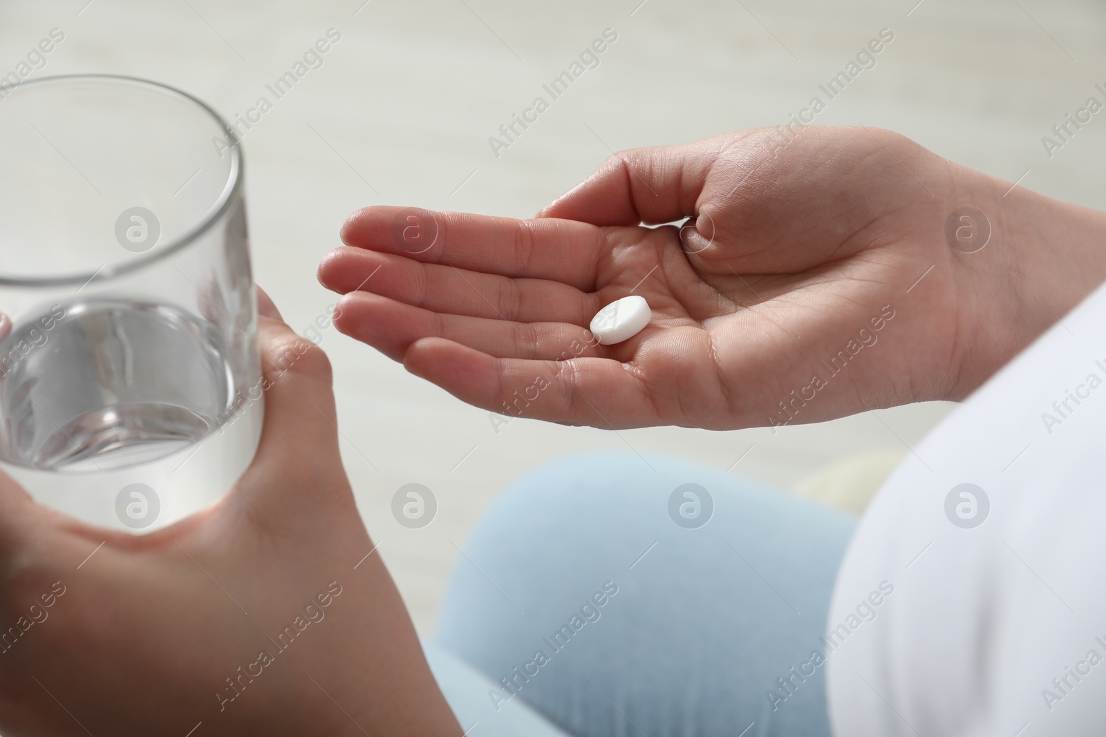 Photo of Woman with glass of water and pill on light background, closeup