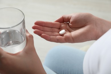 Woman with glass of water and pill on light background, closeup