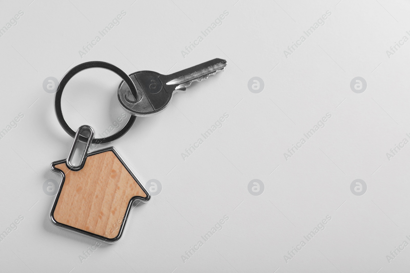 Photo of Key with trinket in shape of house on white background, top view and space for text. Real estate agent services