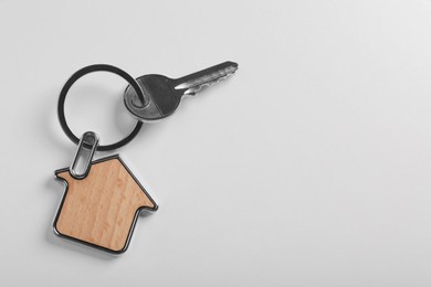 Key with trinket in shape of house on white background, top view and space for text. Real estate agent services