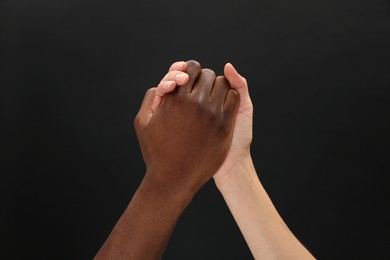 Photo of Woman and African American man clasping hands on black background, closeup
