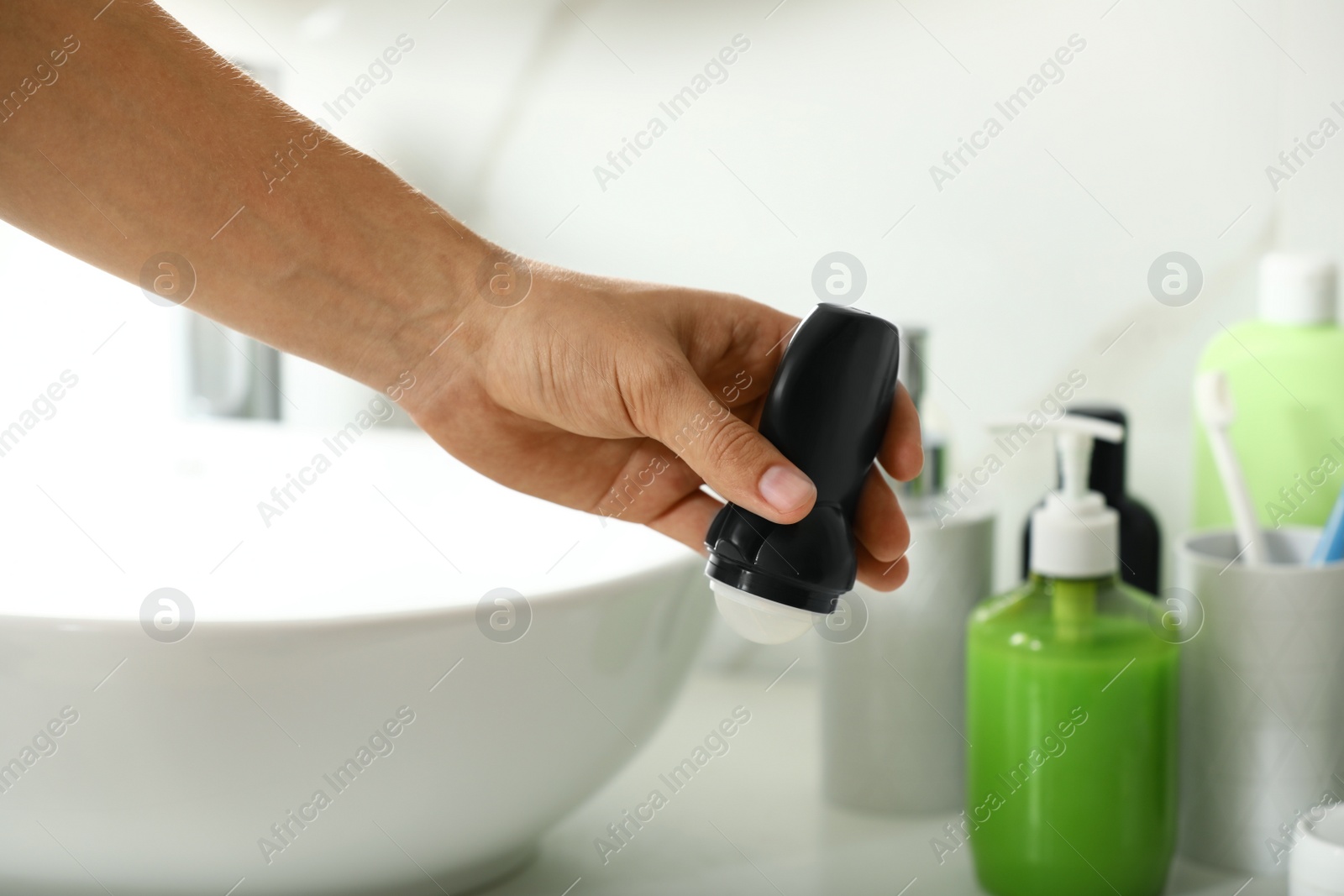 Photo of Man holding roll-on deodorant in bathroom, closeup view