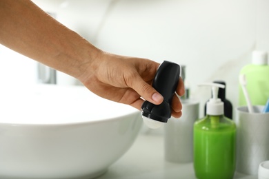 Photo of Man holding roll-on deodorant in bathroom, closeup view