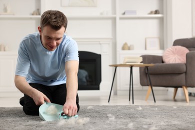 Photo of Smiling man with brush and pan removing pet hair from carpet at home. Space for text