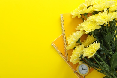 Photo of Beautiful flowers, notebooks and alarm clock on yellow background, flat lay with space for text. Teacher's Day