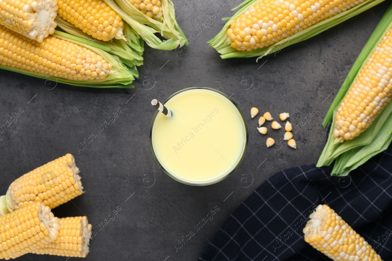 Photo of Corn juice and cobs on black slate background, flat lay