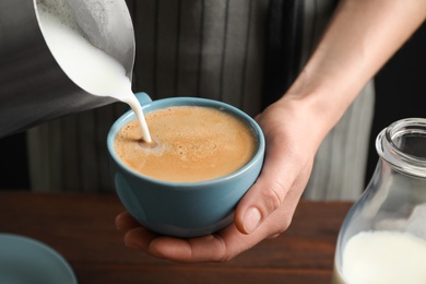 Photo of Woman pouring milk into cup of hot coffee, closeup