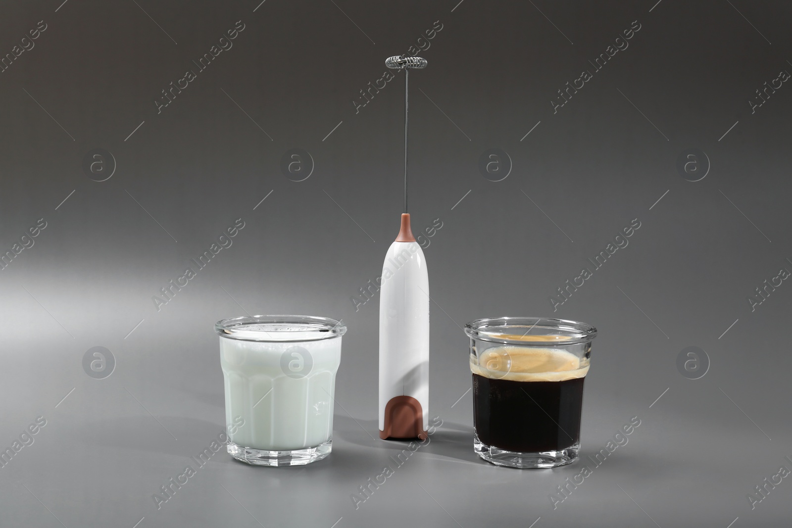 Photo of Mini mixer (milk frother) between glasses of coffee and milk on grey background