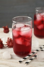 Photo of Delicious hibiscus tea with ice cubes and straws on white wooden table, closeup