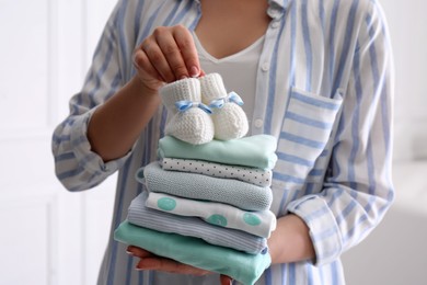 Photo of Woman holding stack of baby's clothes and small booties indoors, closeup