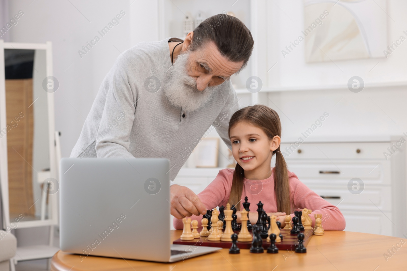 Photo of Grandfather teaching his granddaughter to play chess following online lesson at home