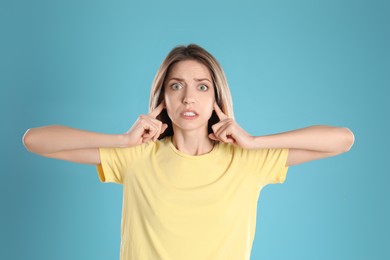 Emotional young woman covering her ears with fingers on light blue background