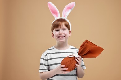 Photo of Easter celebration. Cute little boy with bunny ears and wrapped egg on dark beige background