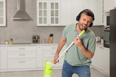 Happy man in headphones with mop singing while cleaning in kitchen. Space for text