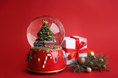 Photo of Beautiful snow globe and Christmas decor on red background