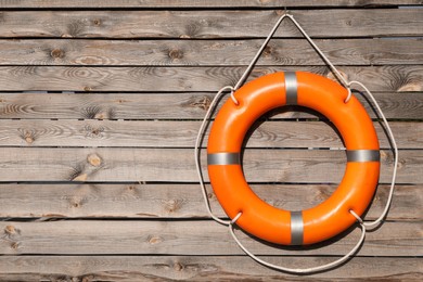 Orange life buoy hanging on wooden wall, space for text