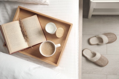 Photo of Cup of aromatic coffee, book and candle on bed with soft blanket indoors, top view