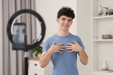 Photo of Smiling teenage blogger explaining something while streaming at home