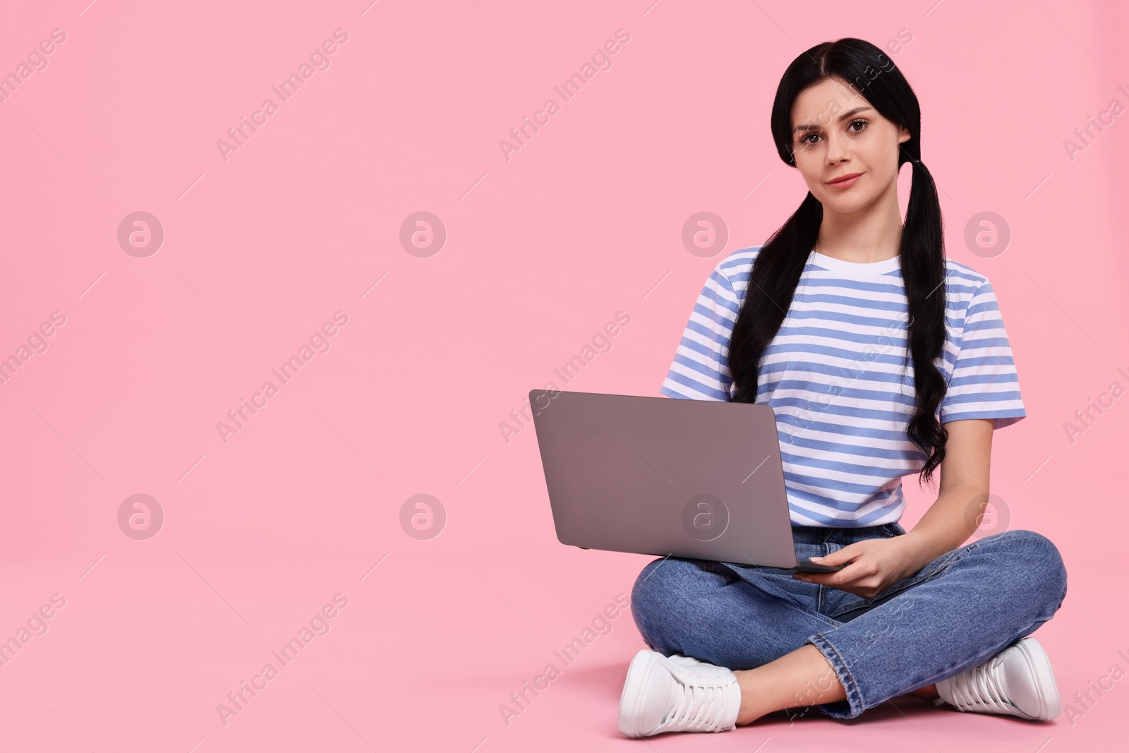 Photo of Student with laptop sitting on pink background. Space for text