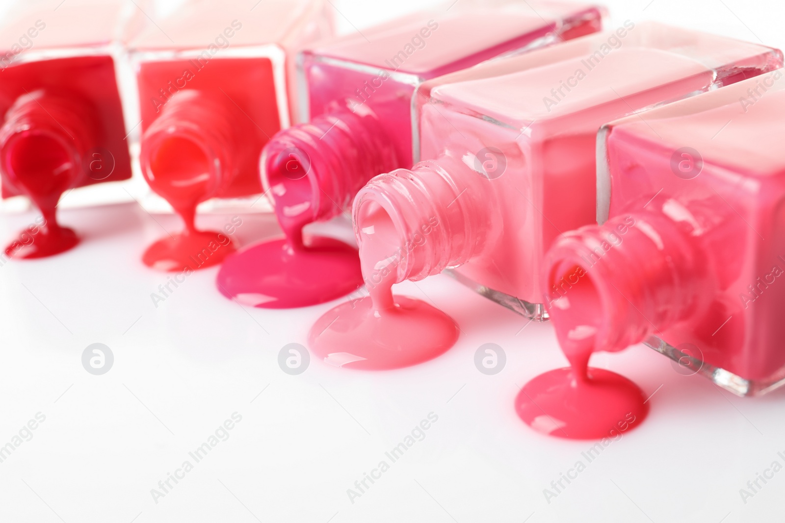 Photo of Spilled different nail polishes with bottles on white background, closeup