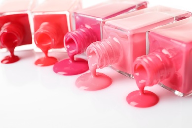 Spilled different nail polishes with bottles on white background, closeup