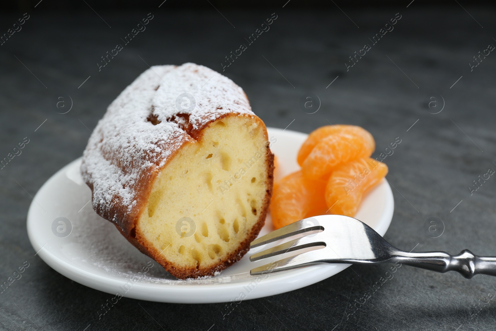 Photo of Piece of delicious homemade yogurt cake with powdered sugar and tangerines on gray table