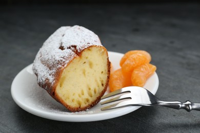 Photo of Piece of delicious homemade yogurt cake with powdered sugar and tangerines on gray table