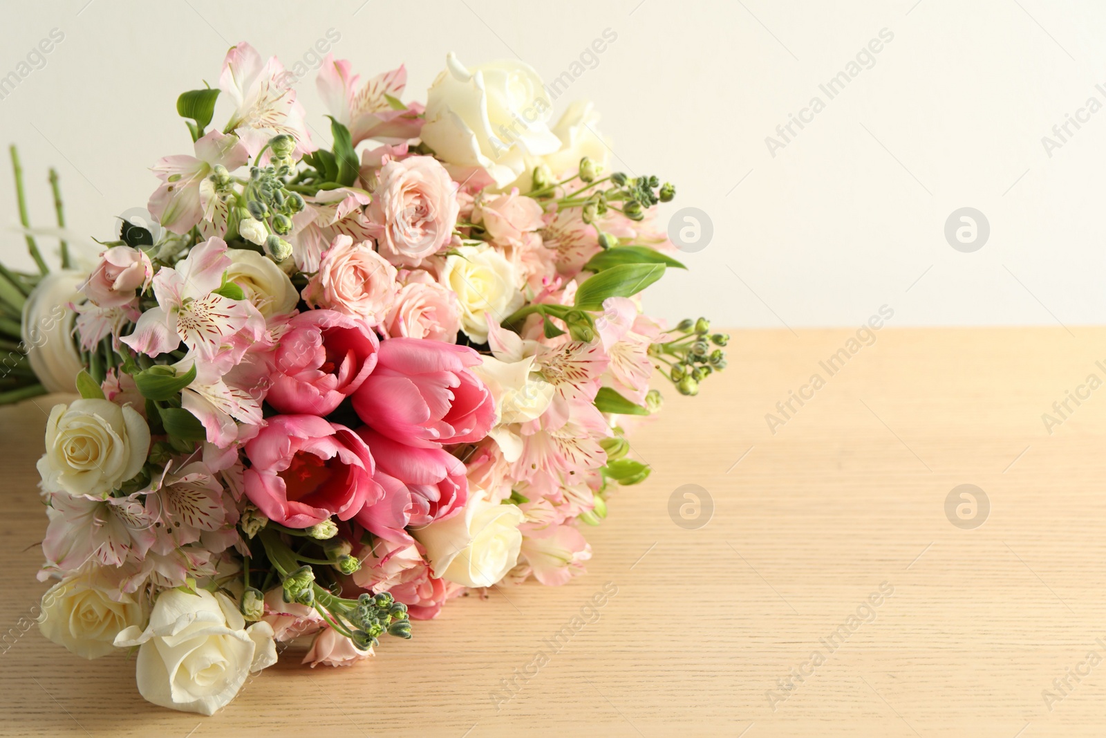 Photo of Beautiful bouquet of fresh flowers on wooden table near light wall. Space for text