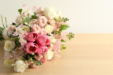 Beautiful bouquet of fresh flowers on wooden table near light wall. Space for text