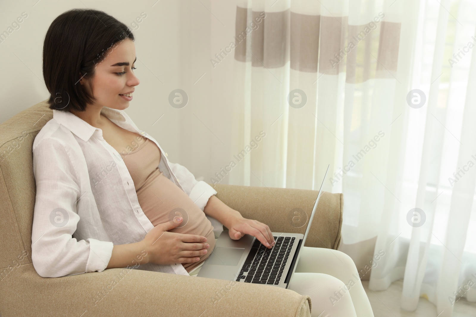 Photo of Pregnant young woman with laptop at home, space for text