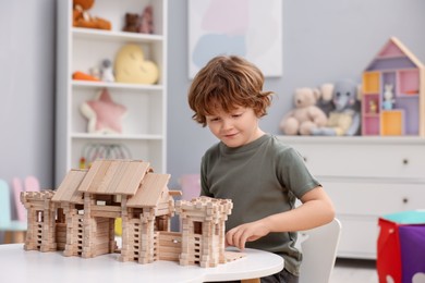 Photo of Little boy playing with wooden entry gate at white table in room. Child's toy