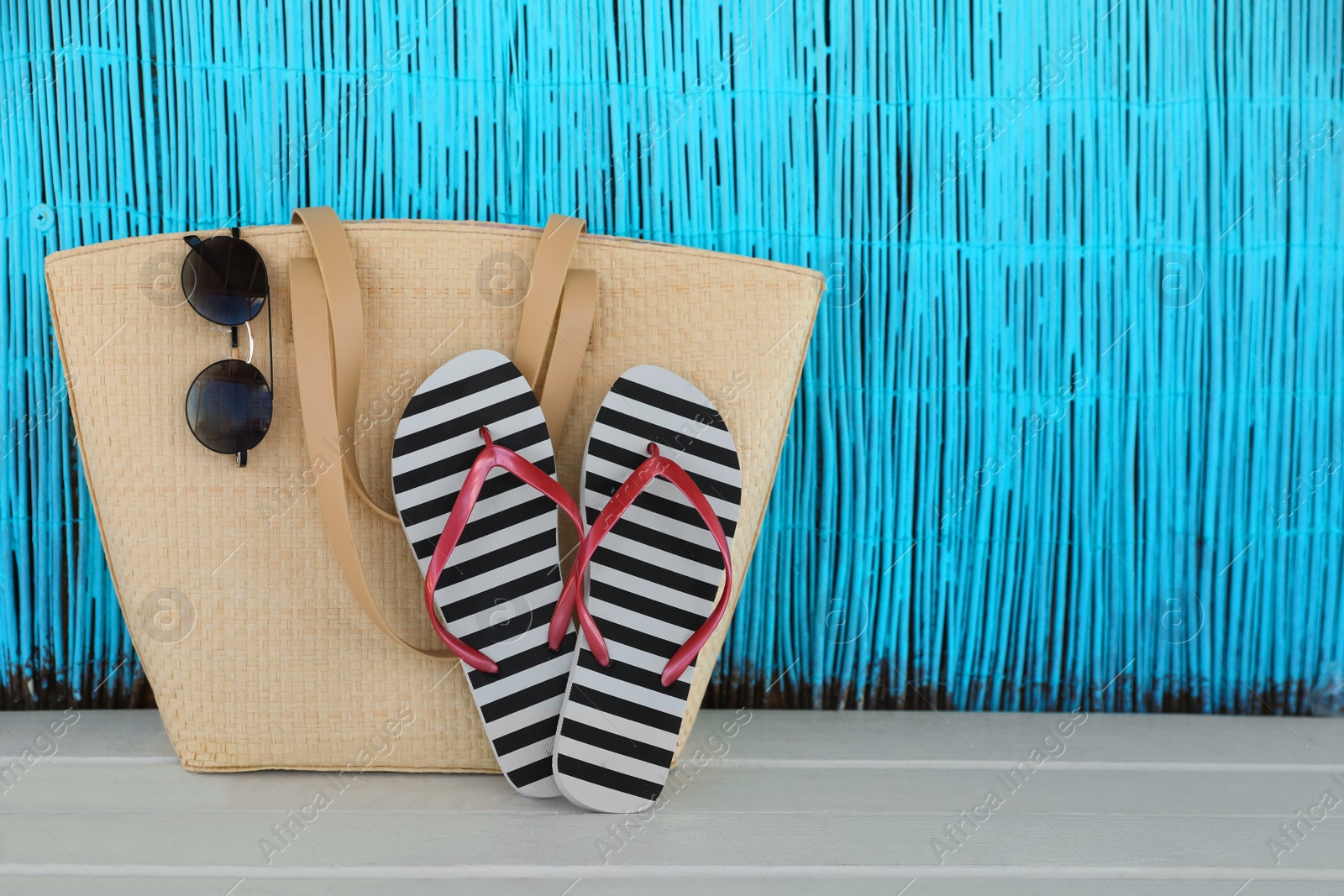 Photo of Stylish flip flops, bag and sunglasses on white wooden table. Space for text