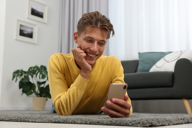 Photo of Happy young man having video chat via smartphone on carpet indoors