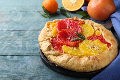 Photo of Delicious galette with citrus fruits and rosemary on blue wooden table