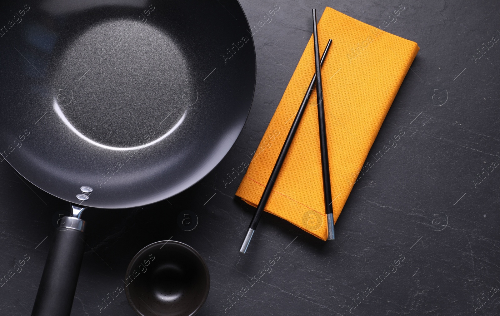 Photo of Empty iron wok, sauce bowl and chopsticks on black table, flat lay