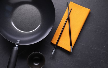 Empty iron wok, sauce bowl and chopsticks on black table, flat lay