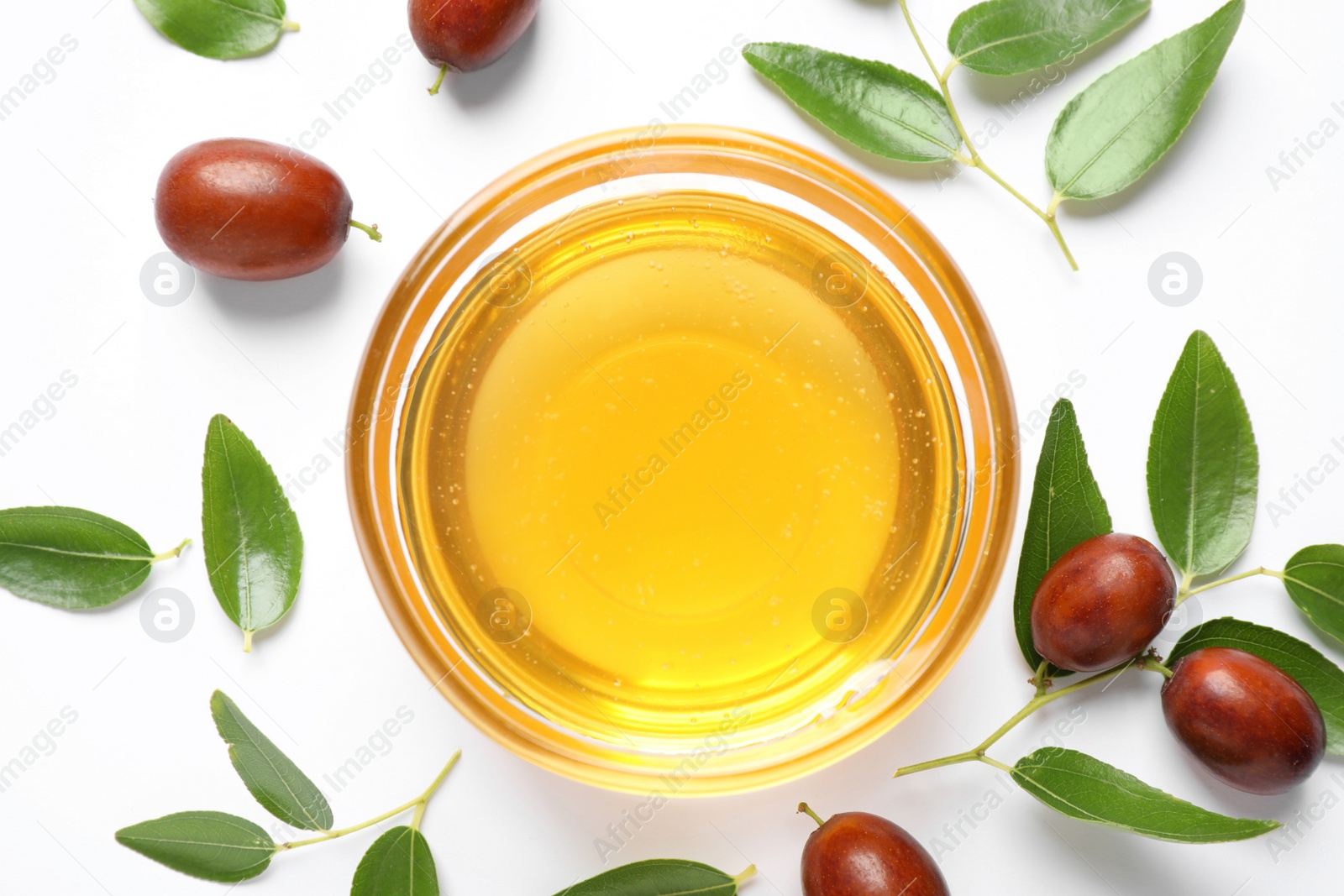 Photo of Glass bowl with jojoba oil and seeds on white background, top view