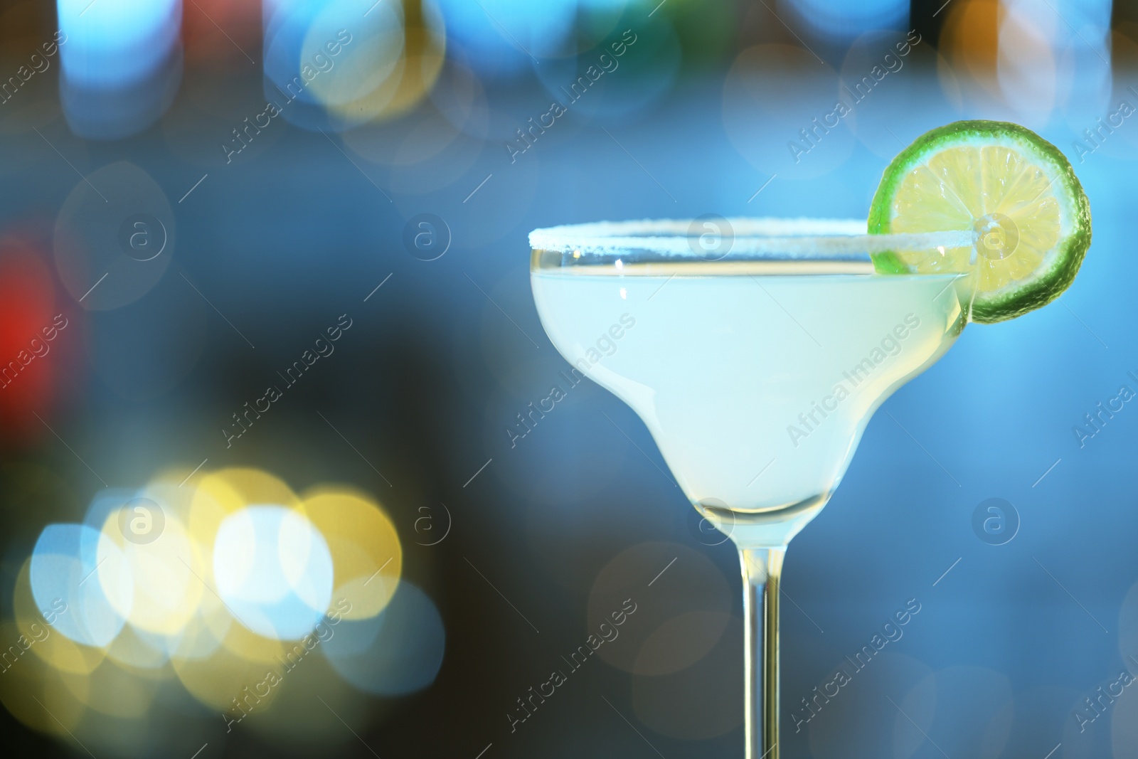 Photo of Glass of fresh alcoholic cocktail against blurred background. Space for text