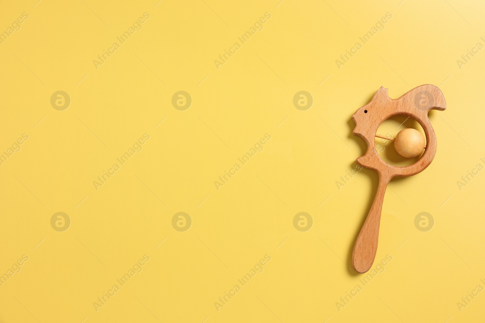 Photo of Baby accessories. Wooden rattle on yellow background, top view. Space for text