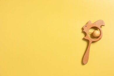 Photo of Baby accessories. Wooden rattle on yellow background, top view. Space for text